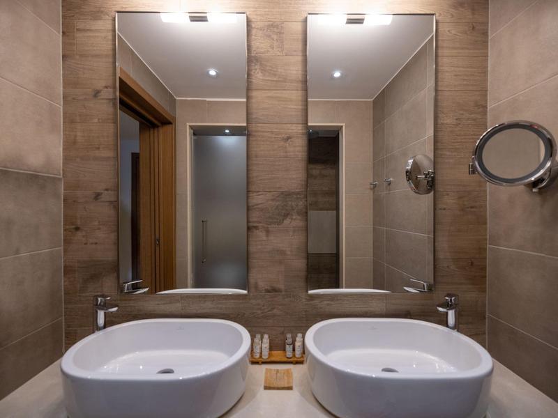 Moderní koupelna se dvěma bílými umyvadly, velkými zrcadly a béžovými obklady na stěnách.