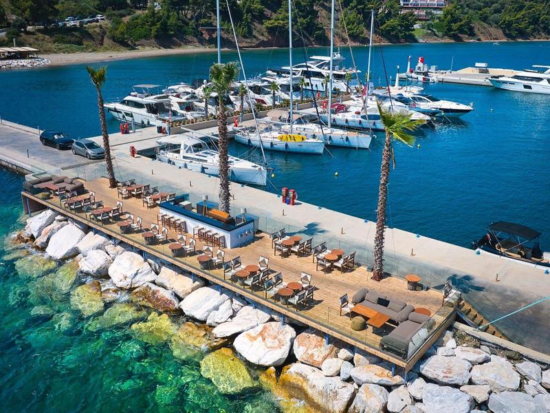 Marina s jachtami a loděmi zakotvenými podél kamenného mole s průzračnou tyrkysovou vodou.