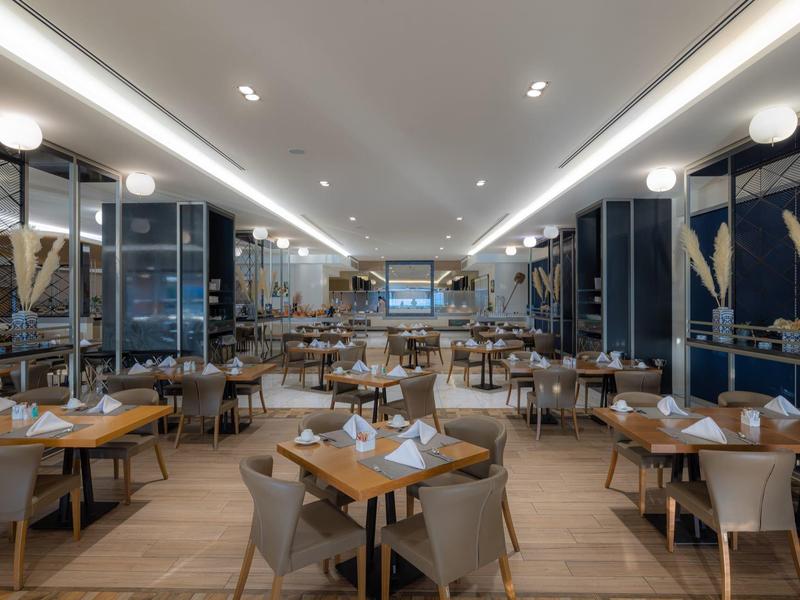 Prostorná moderní hotelová restaurace s dřevěnými stoly, béžovými židlemi a teplým osvětlením.