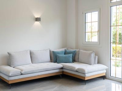 Helle Wohnzimmer-Ecke mit grauem Stoffsofa, blauen Kissen, weißer Wand und großem Fenster.