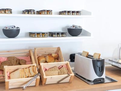 Buffet mit frischem Brot, Brötchen, Toaster und Müslischalen auf hellem Holzuntergrund.