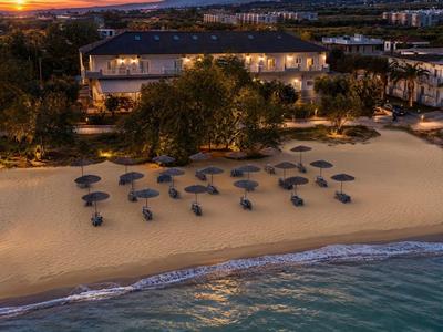 Sonnenuntergang am Strand mit Hotel und vielen Sonnenschirmen in einer ruhigen Bucht.