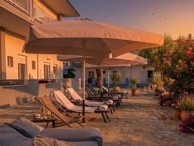 Sonnenschirme und Liegestühle auf Steinmauerterrasse bei Sonnenuntergang am Hotel.