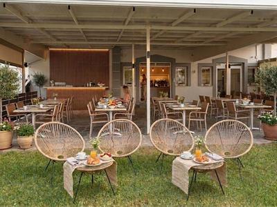 Eine Hotelterrasse mit runden Stühlen, Tischen und grüner Rasenfläche bei Tageslicht.