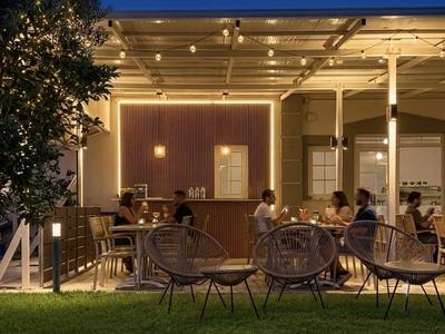 Offene Terrasse mit dekorativer Beleuchtung und Gästen an Tischen in einem Außenbereich eines Hotels.