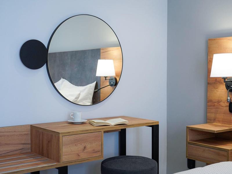 Nowoczesna część pokoju hotelowego z okrągłym lustrem, drewnianymi meblami i stołkiem