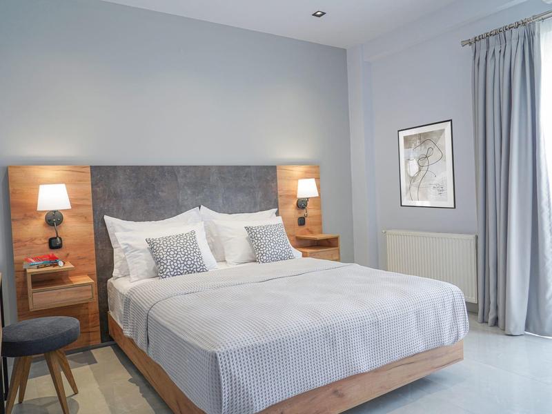 Nowoczesny pokój hotelowy z dużym łóżkiem podwójnym, szafkami nocnymi i jasnymi zasłonami.