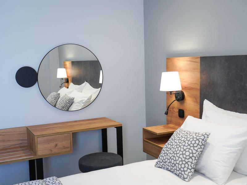 Nowoczesny pokój hotelowy z okrągłym lustrem, drewnianymi meblami i wygodnym łóżkiem z poduszkami