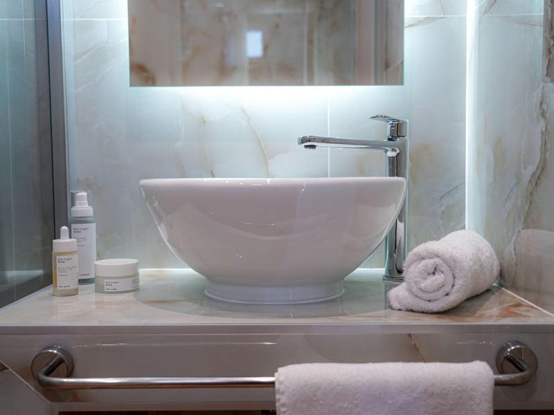 Nowoczesna łazienka z owalną umywalką, lustrem na ścianie i białymi ręcznikami.