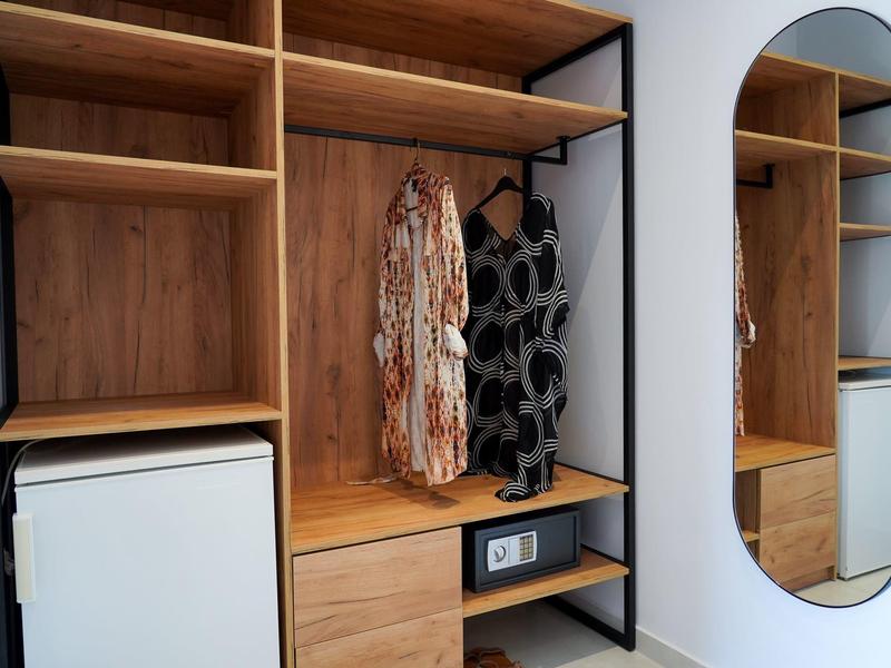 Otwarta drewniana szafa z lustrem i dwoma sukienkami w pokoju hotelowym.