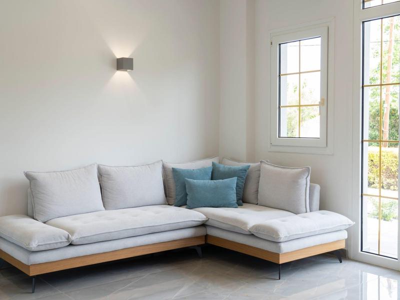 Nowoczesny salon z jasnoszarym narożnikiem i dużymi oknami zapewniającymi dużo światła dziennego.