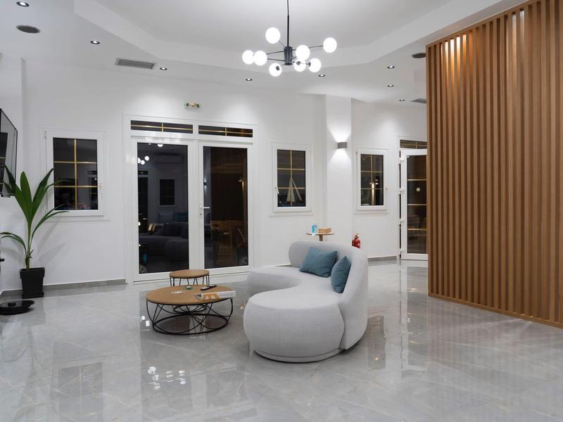 Nowoczesna strefa wypoczynkowa hotelu z jasnymi meblami, szklanymi drzwiami i drewnianą ścianką.