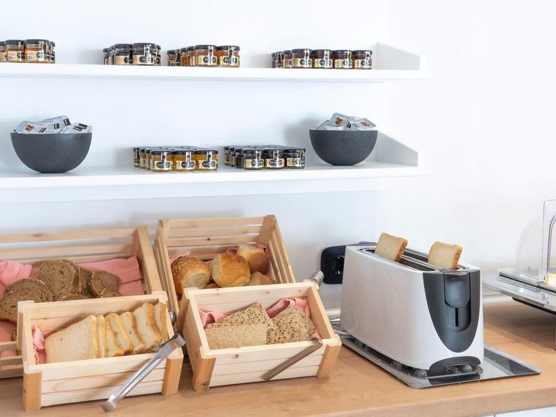 Bufet śniadaniowy z koszykami na pieczywo, tosterem i małymi miseczkami z pastami.