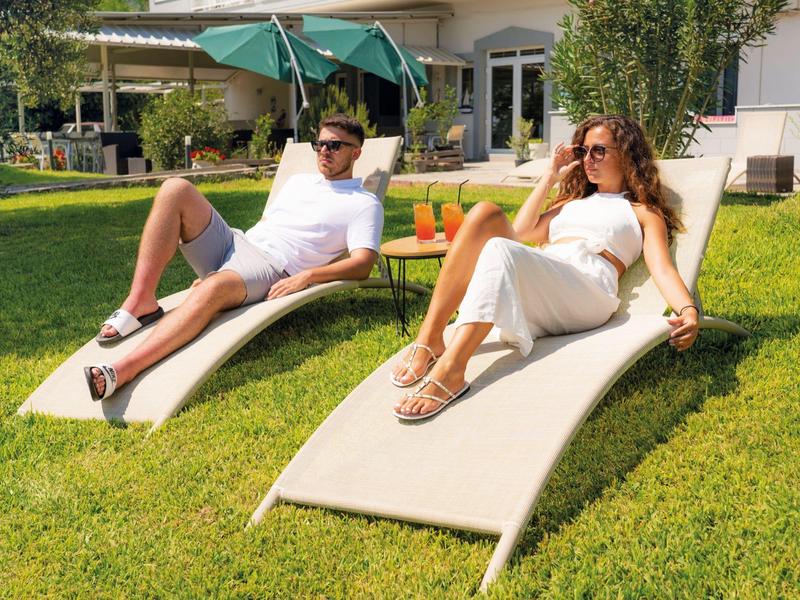 Dwie osoby relaksują się na leżakach w ogrodzie domu podczas słonecznego dnia.