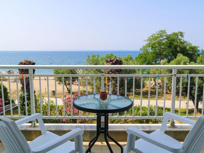 Balkon z stołem i dwoma krzesłami z widokiem na ogród i morze pod czystym niebem.
