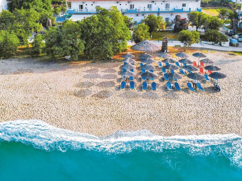 Plaża z parasolami i leżakami przed białym budynkiem i zielonym tłem