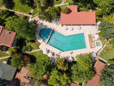 Aerial view of a hotel pool with sun loungers surrounded by trees and buildings.