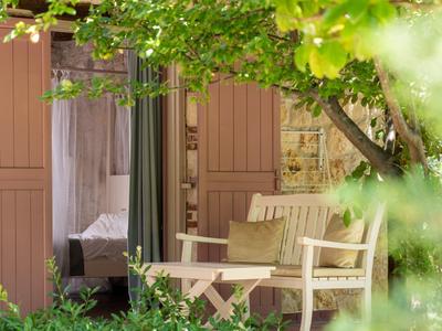Cozy patio with table and chairs in front of a room, surrounded by green plants.