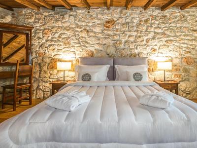 Cozy bed with white bedding and pillows against a rustic stone wall in a hotel room.