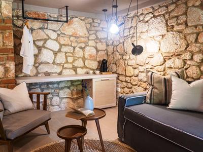 Cozy room with stone walls, sofa, armchairs, and wooden tables in warm lighting.