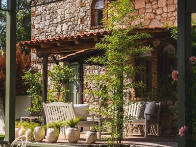 A rustic stone house with seating area and climbing plants on the terrace.