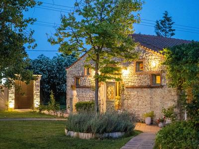 Lit stone house with garden and trees at dusk.