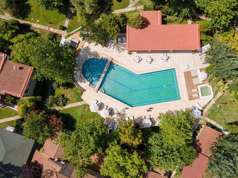 Aerial view of a hotel pool with sun loungers surrounded by trees and buildings.