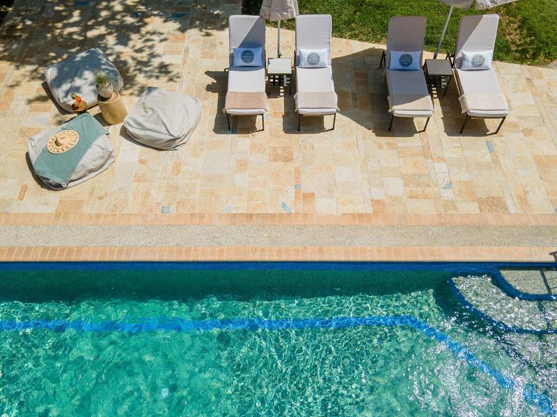 Pool area with blue water, sun loungers, white umbrellas, and shaded spots.