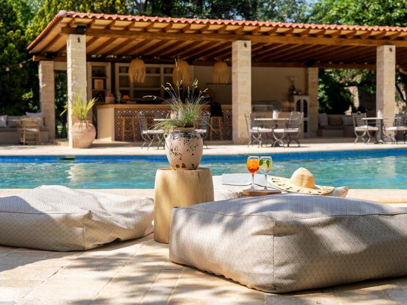 Cozy outdoor lounge with pool, wildflowers, and cocktails in a sunny vacation setting.