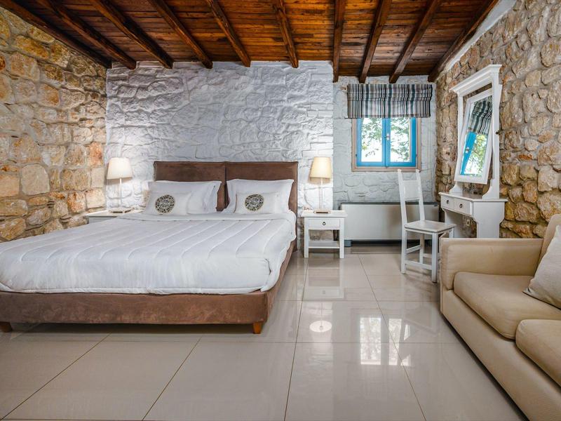 Bedroom with stone wall background, double bed, sofa, and window with curtain.