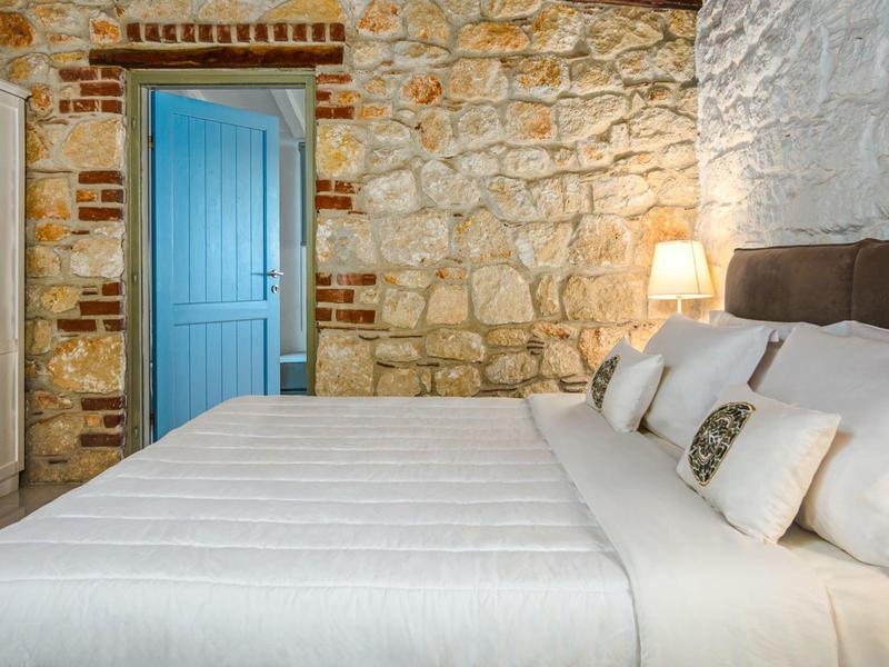 Cozy bedroom with exposed stone wall and blue door, bed with white and patterned pillows.