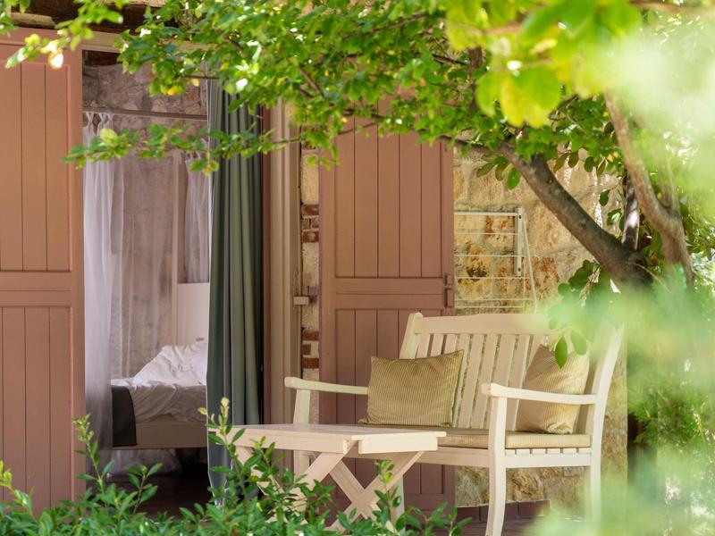 Cozy patio with table and chairs in front of a room, surrounded by green plants.