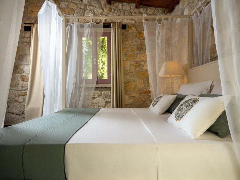 Cozy bedroom with canopy bed, stone wall, and natural light.