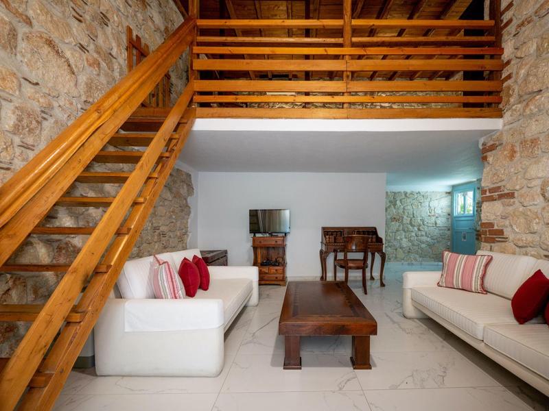 Cozy living room with white sofas, wooden table, wooden staircase, and stone walls.