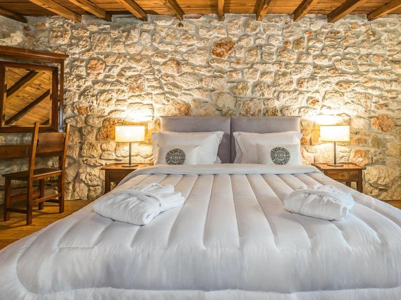 Cozy bed with white bedding and pillows against a rustic stone wall in a hotel room.