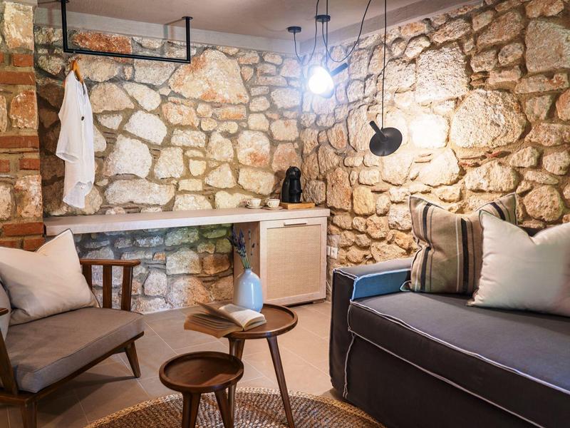 Cozy room with stone walls, sofa, armchairs, and wooden tables in warm lighting.