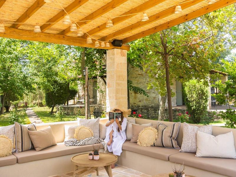 Covered terrace with seating area and wooden tables, surrounded by green trees.