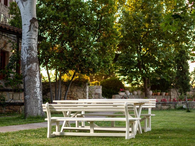 White picnic table with benches on grassy area under trees in garden.