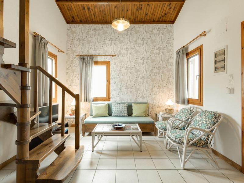 Soggiorno luminoso con divano, poltrone, tavolino in legno e scala a chiocciola.