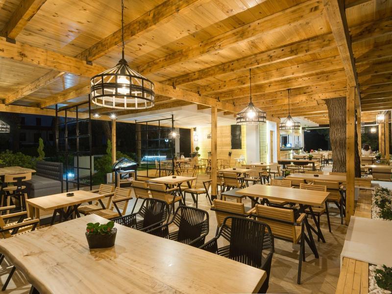 Terrazza di ristorante in legno con tavoli, sedie e illuminazione calda di sera.