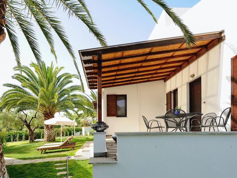 Terrazza di villa con mobili in metallo e palme in giardino curato.