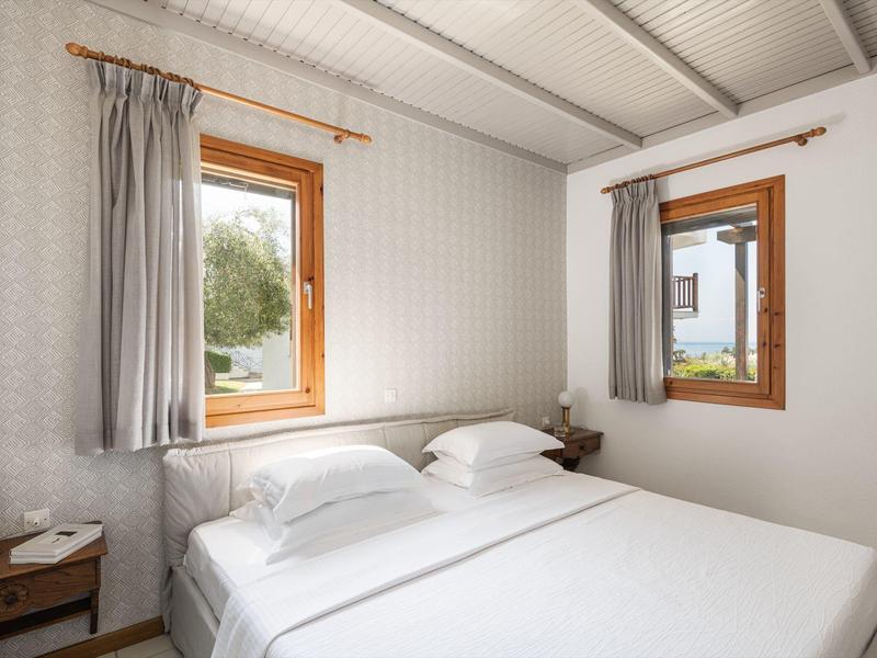 Camera d'albergo luminosa con letto bianco grande e due finestre incorniciate in legno.