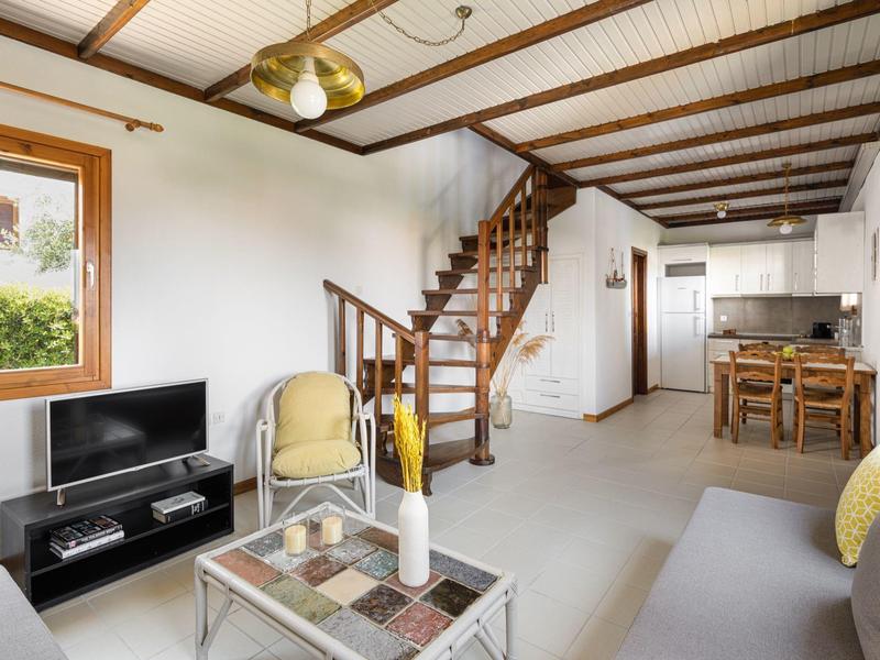 Soggiorno luminoso con divano, TV, poltrona, scala in legno e zona pranzo sullo sfondo.