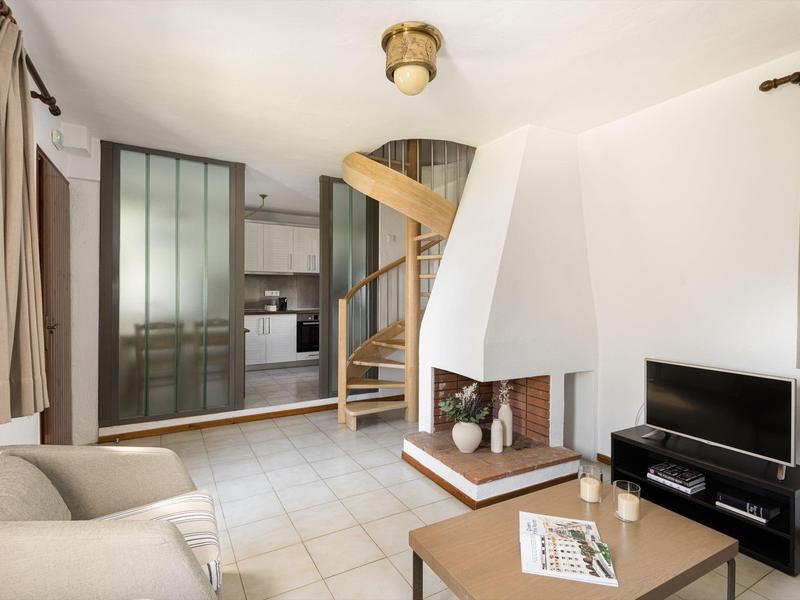 Soggiorno moderno con divano beige, scala a chiocciola e cucina a vista.