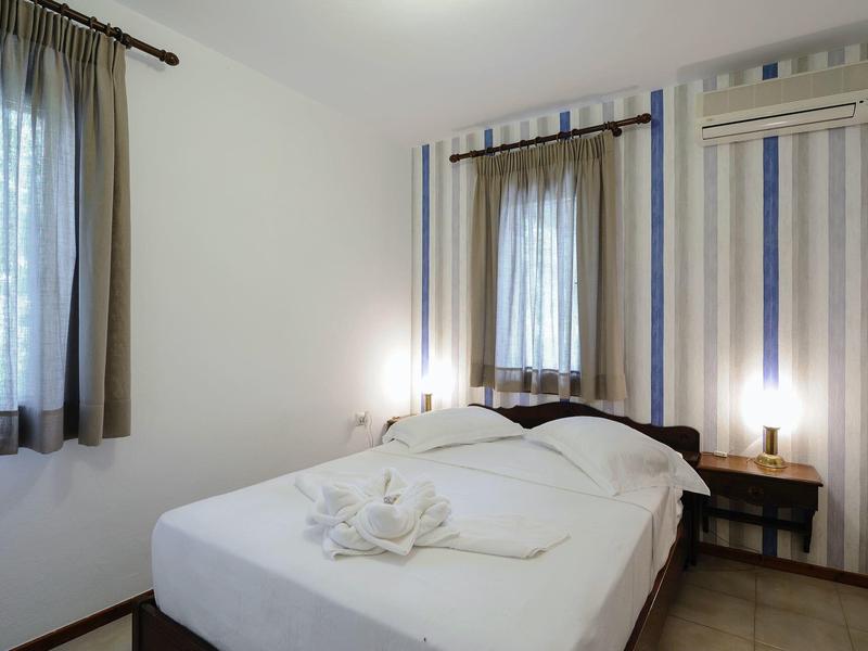 Camera d'albergo semplice con letto matrimoniale, finestre con tende e aria condizionata a muro.