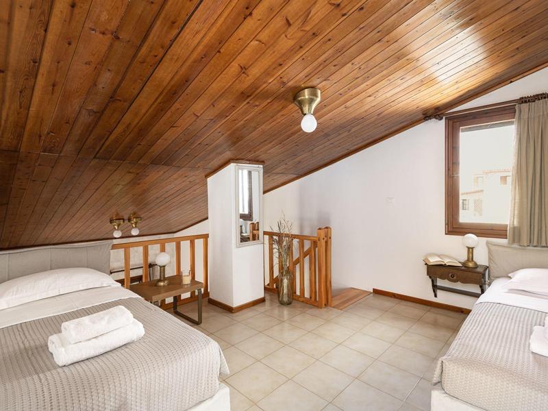 Camera mansardata con due letti singoli, biancheria bianca, soffitto in legno e finestra.