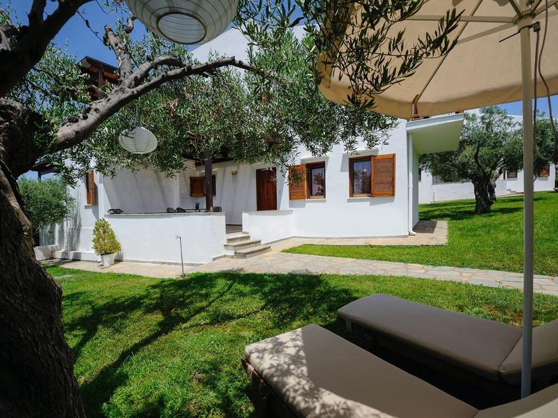 Giardino verde con ombrellone e casa bianca sullo sfondo sotto un cielo blu.