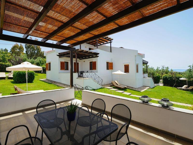 Casa bianca con terrazza, mobili da giardino in metallo nero, prato curato e ombrellone.