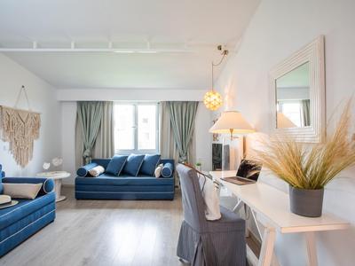 Jasny salon z niebieskimi sofami, biurkiem i dekoracyjnymi roślinami w pokoju hotelowym.