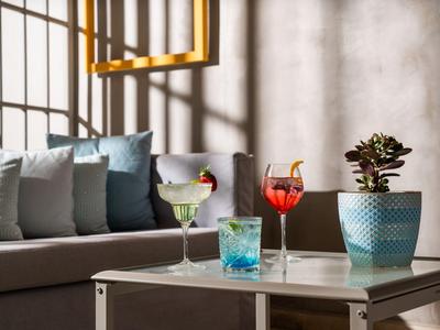 Trzy kolorowe koktajle na stole obok sofy z poduszkami i rośliną w doniczce